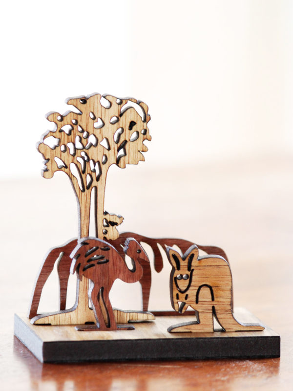 A wooden mini landscape of an Australian image with Uluru, a kangaroo, an emu and a koala in a gum tree. Four wooden images sit into a wooden base to make up the 3D landscape.