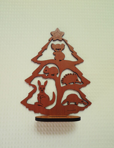 A wooden Australian made Christmas tree. It is a cut out of a tree with a koala, a wombat, an echidna, a kangaroo and a platypus in it and it stands on a little wooden stand.