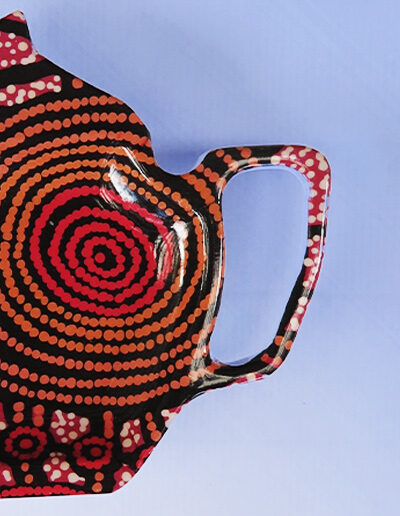 A close up of a melamine tea bag holder in the shape of a teapot. The pattern on it is artwork by Teddy Gibson