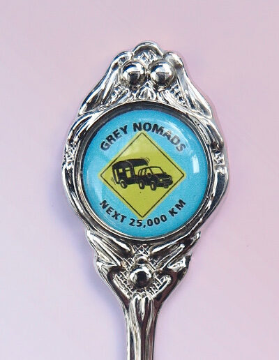 The crest of a souvenir spoon with the Grey Nomads caravanning on it.