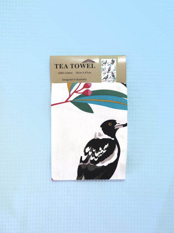 A cream cotton tea towel with Magpie images printed on it.