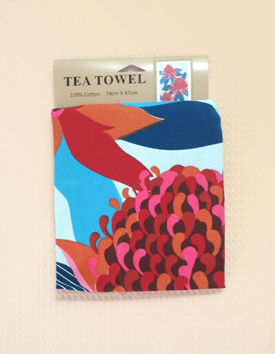 A pale blue cotton tea towel with a large red Waratah print on it.