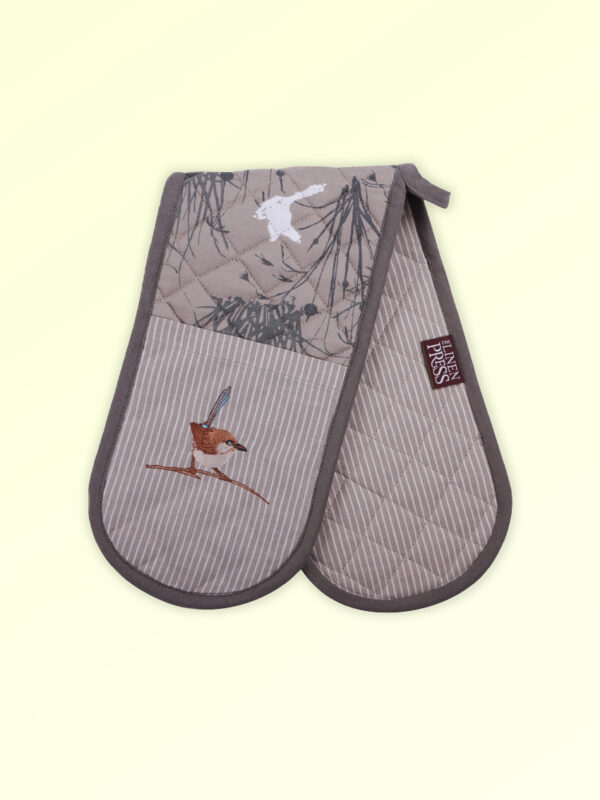 Insulated double oven mitts with an embroidered blue wren perched in grasses as the fabric design. The fabric is a natural Australian organic cotton with brown/grey trim around it and a tab to hang it.