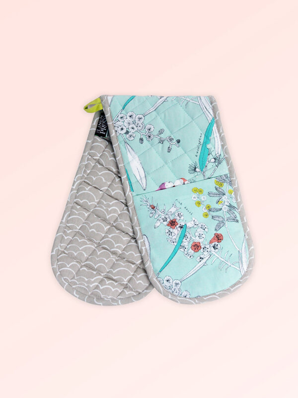 Insulated double oven mitts. The fabric is Australian organic cotton with an aqua background and budgerigars and small native flowers in pastel colours. The trim around it is soft grey with a tab for hanging.