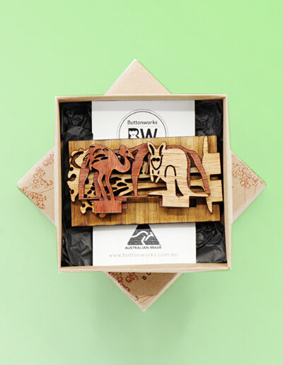 A wooden mini landscape of an Australian image with Uluru, a kangaroo, an emu and a koala in a gum tree. Four wooden pieces sit into a wooden base to make up the 3D landscape. It comes in this recycled card box.