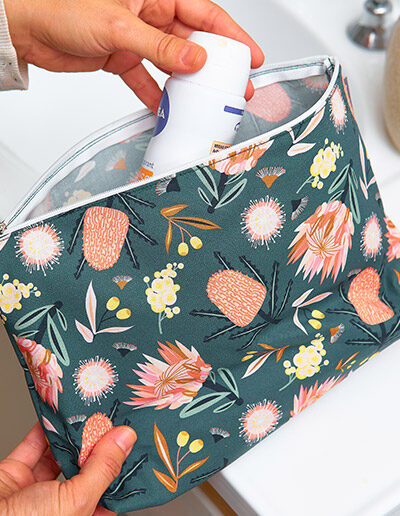 Large cosmetic bag with the Aussie Flora design fabric in khaki, being held to demonstrate an aerosol deodorant fits in it easily.