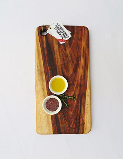 A medium wooden chopping board with a dish of salt & a dish of oil