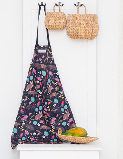 Kitchen apron with the fabric design of Australian nocturnal animals, hanging on a hook next to baskets